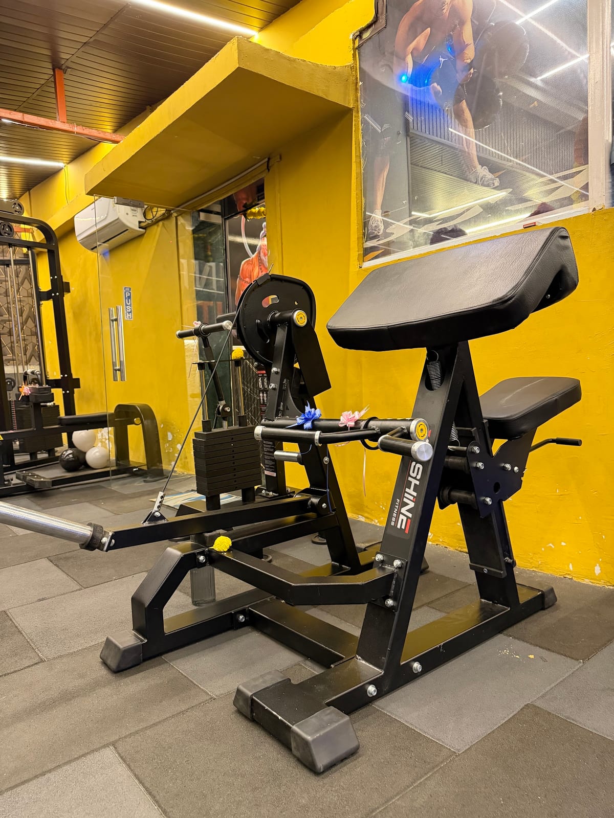 Weight-training machines set against yellow walls and tiled floor in gym interior