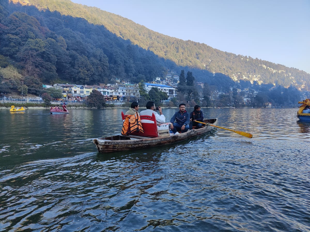 Passengers in a wooden boat crossing a lake near a lakeside settlement
