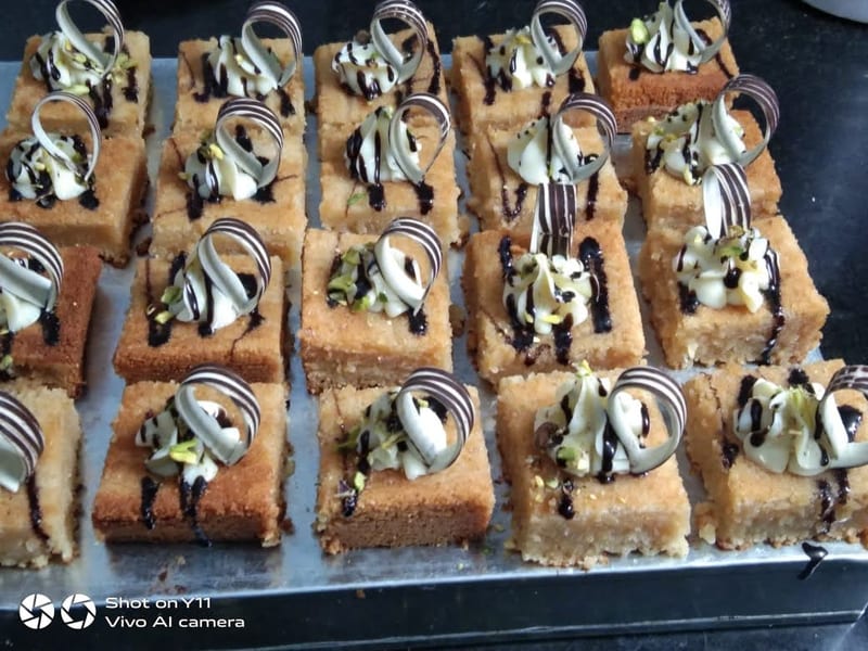 Rows of rectangular pastries topped with cream, chocolate drizzle and pistachios