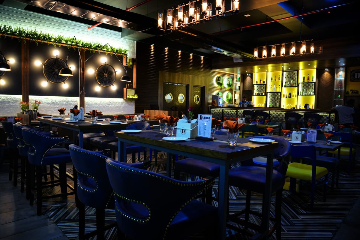 Dimly lit dining area with blue chairs, pendant lights and a backlit bar