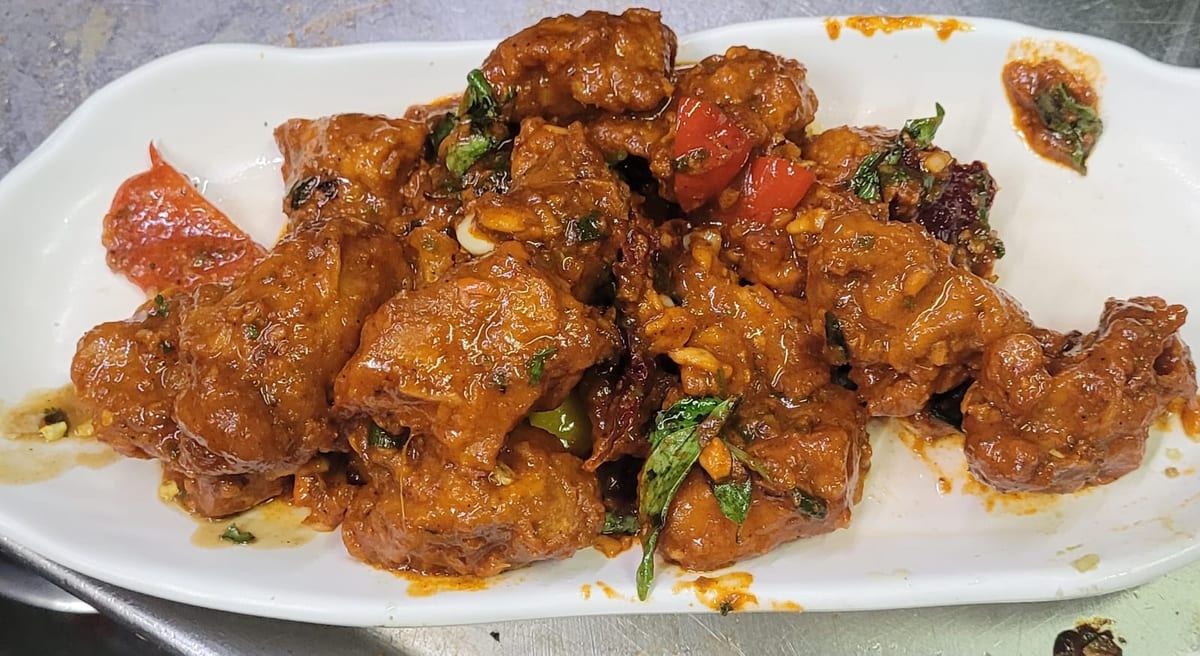 Fried pieces in reddish-brown sauce with herbs and cherry tomatoes on a white plate