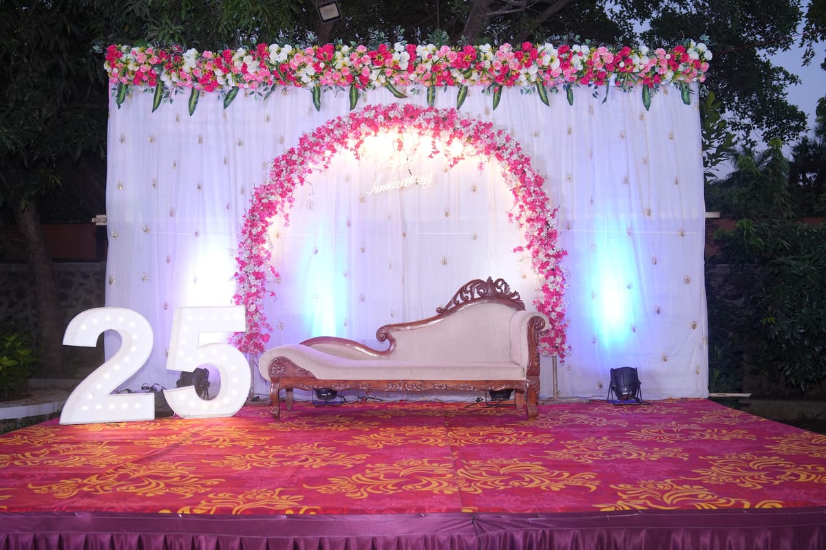 Decorated event stage with floral arch, ornate couch, illuminated backdrop and large number 25