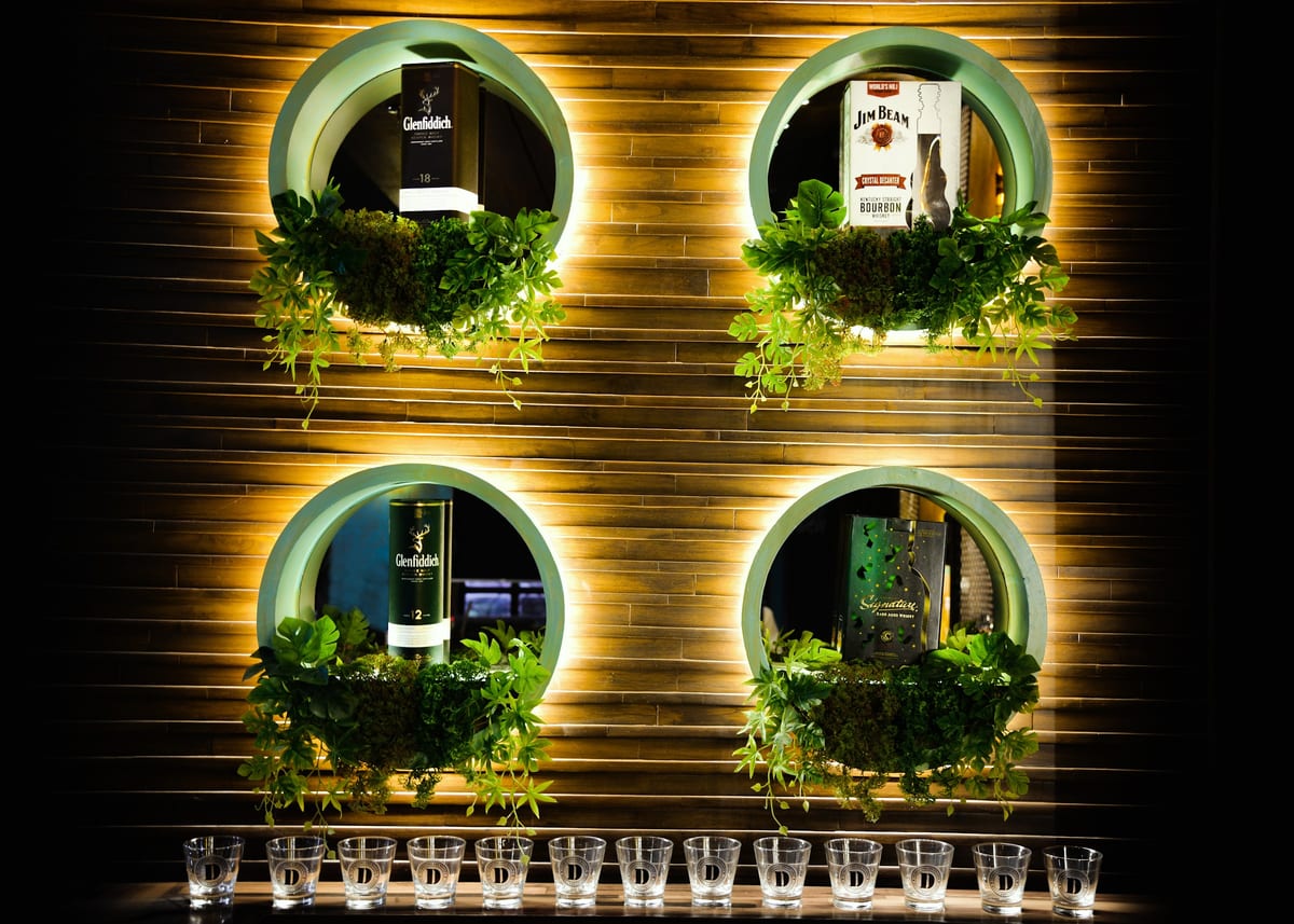 Wood-paneled wall with illuminated bottle displays and rows of tasting glasses