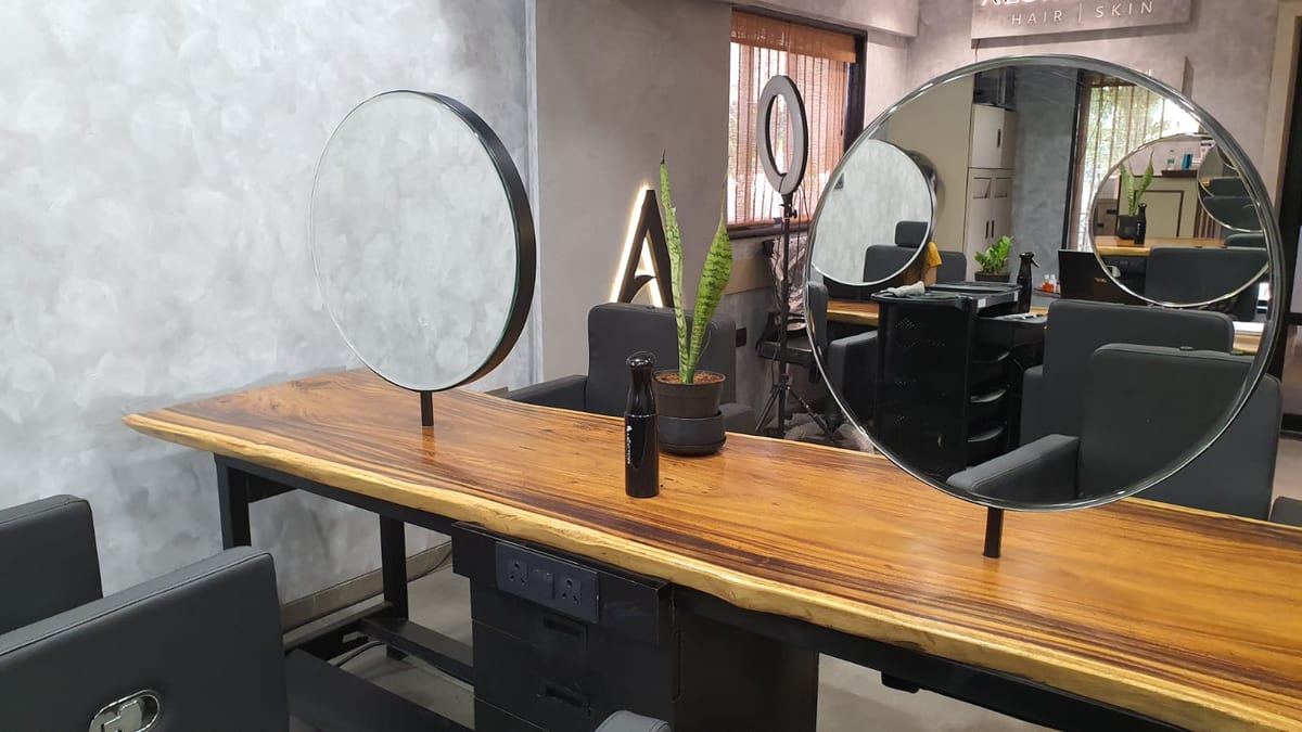 Styling station with wooden counter, round mirrors, salon chairs and plants