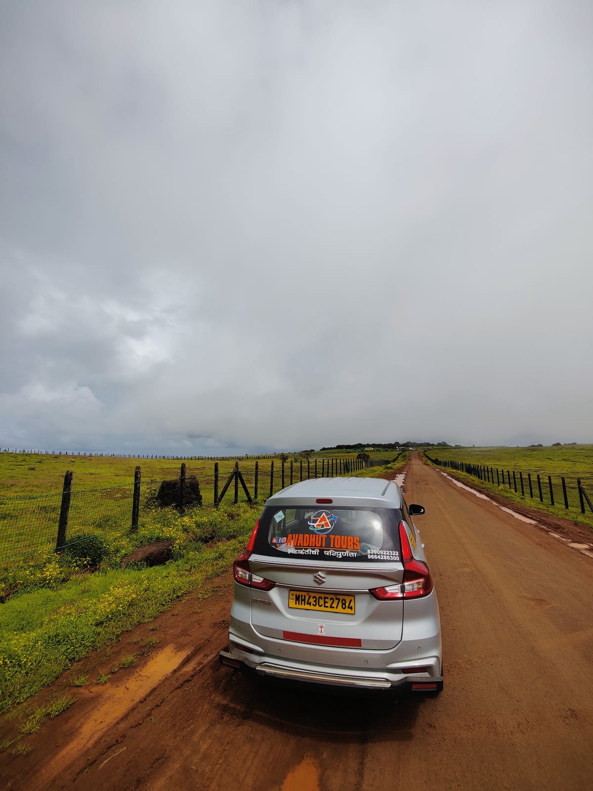 Silver Avadhut Tours car on a dirt road between fenced green fields