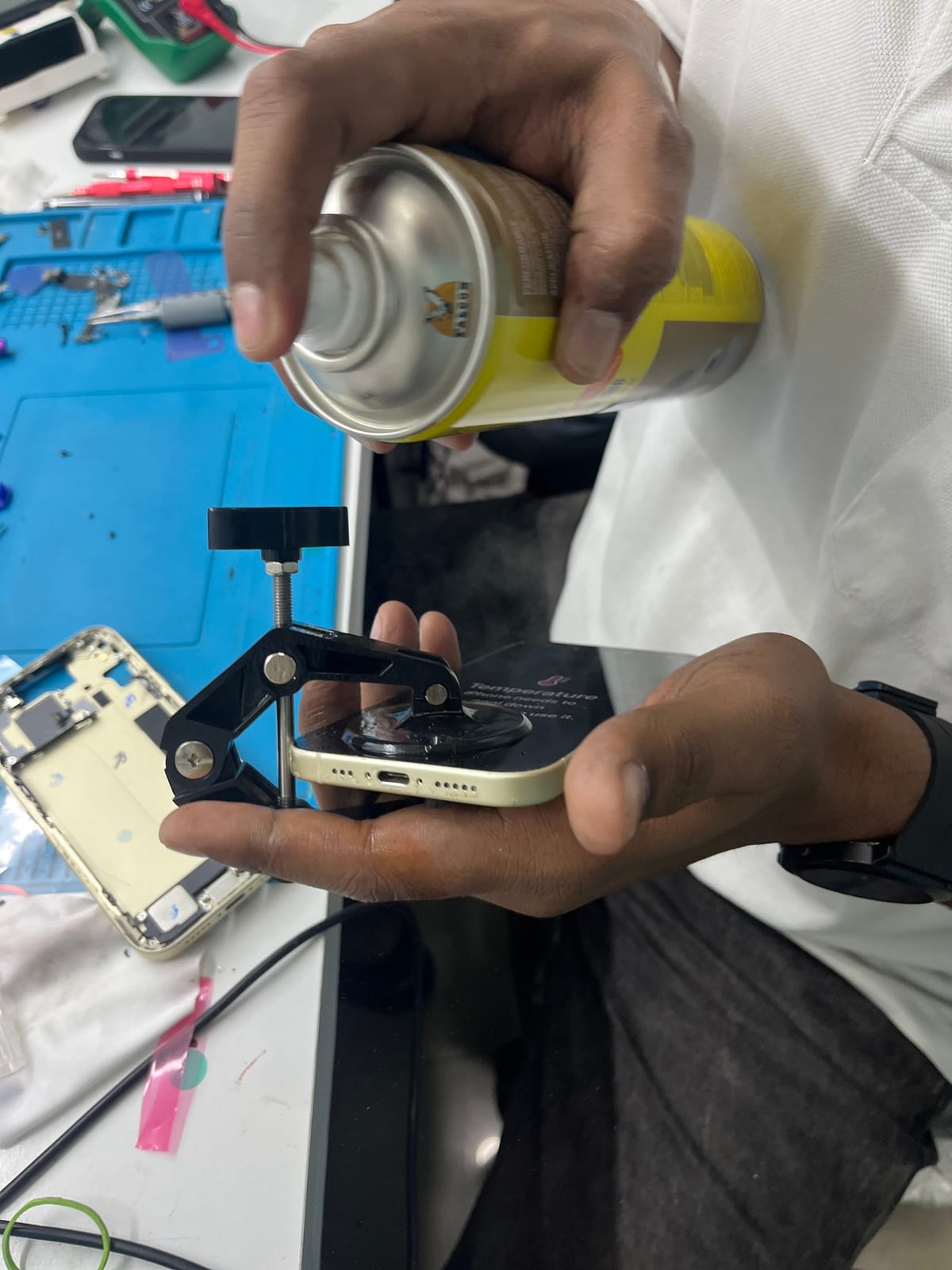 Technician working on a smartphone with a clamp tool and spray can