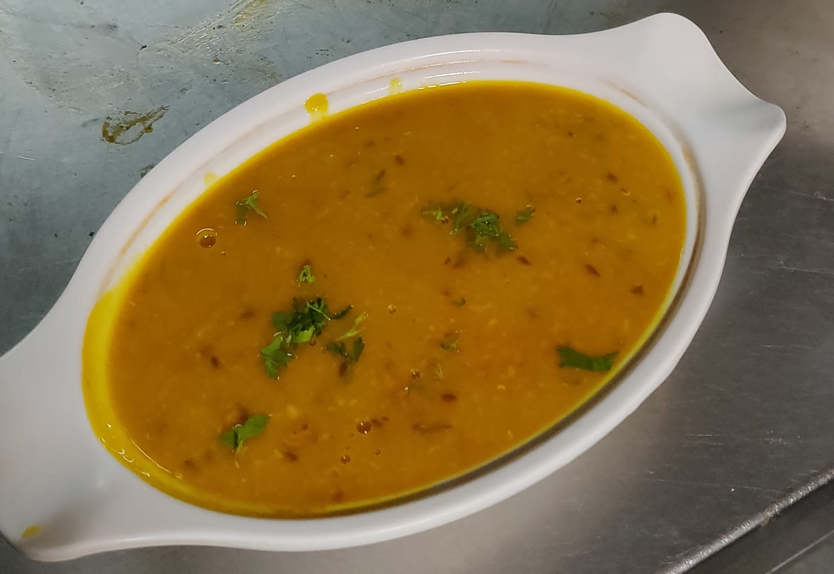 Bowl of orange lentil soup garnished with chopped herbs