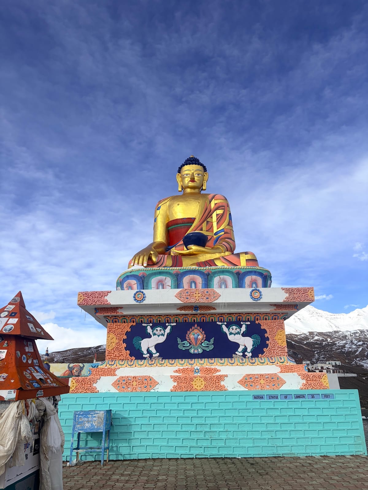 Painted seated statue on an ornate shrine with snowy mountains behind