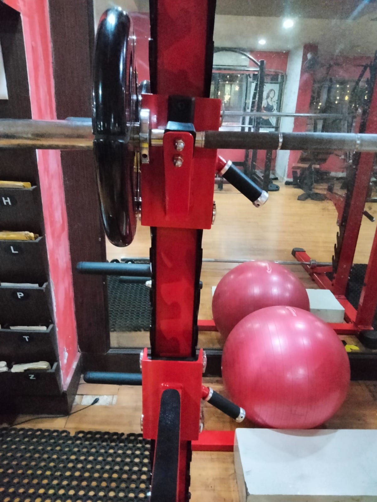 Gym floor with red weight equipment, weight plates, mirrors and pink exercise balls