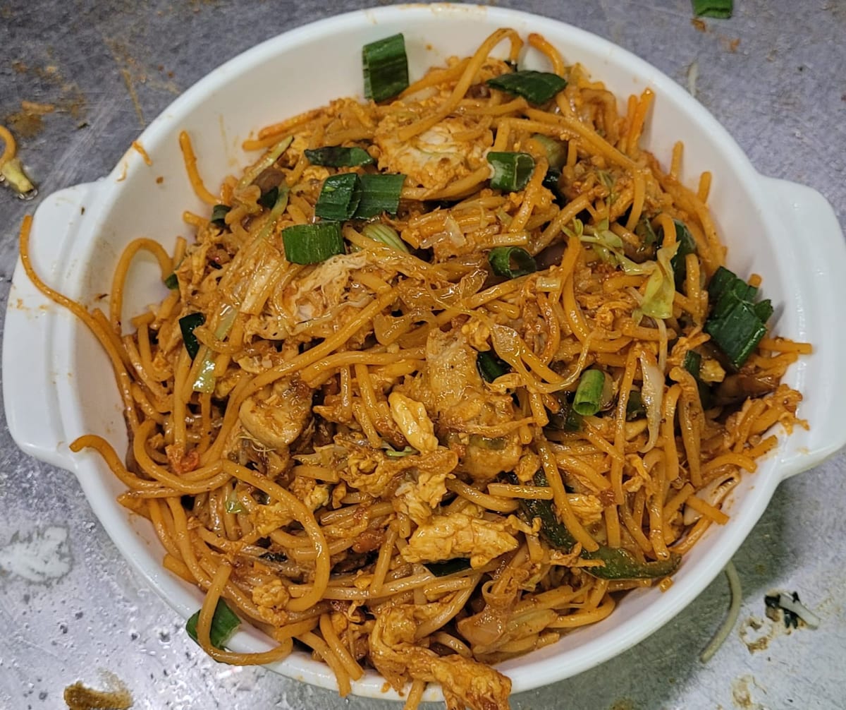 Stir-fried noodles with green vegetables and pieces of meat in a white dish