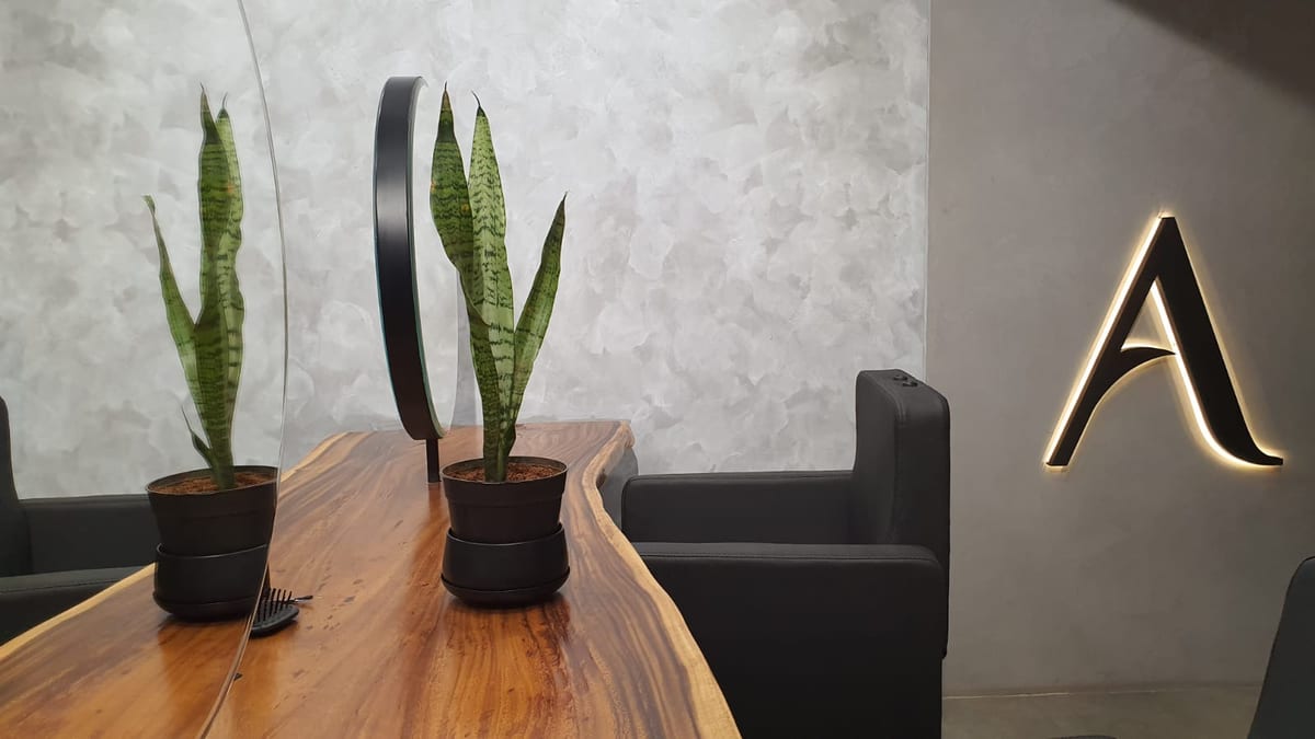 American Hairline reception with a wooden table, snake plants, black chairs and an illuminated letter A sign