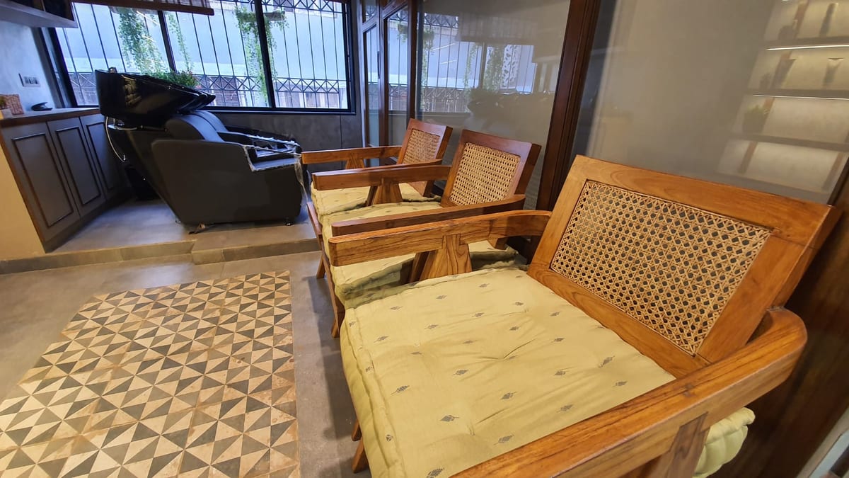 Seating area with wooden cane chairs, a sofa, patterned rug and large windows