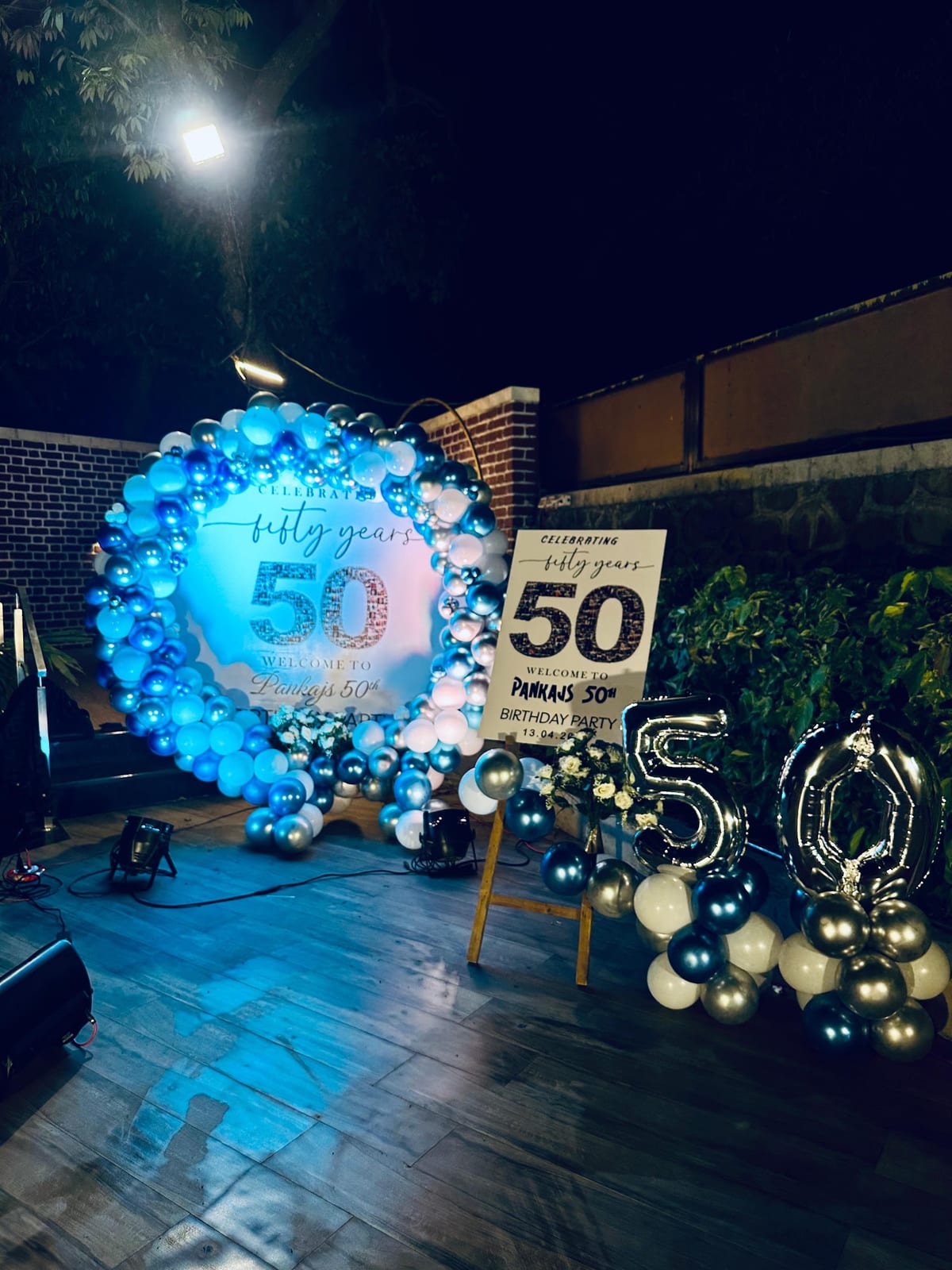 Nighttime anniversary display with blue and white balloons, backdrop and metallic 50 balloons