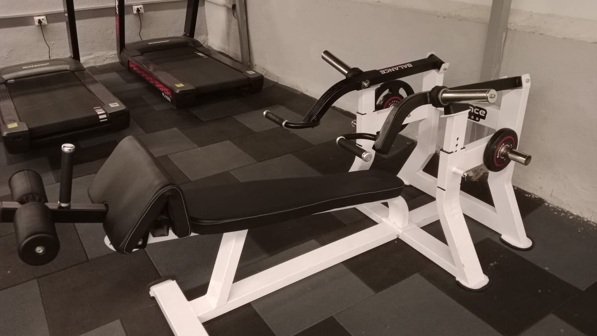 Weight benches, treadmills, and exercise machines on rubber flooring inside Unique Fitness Gym