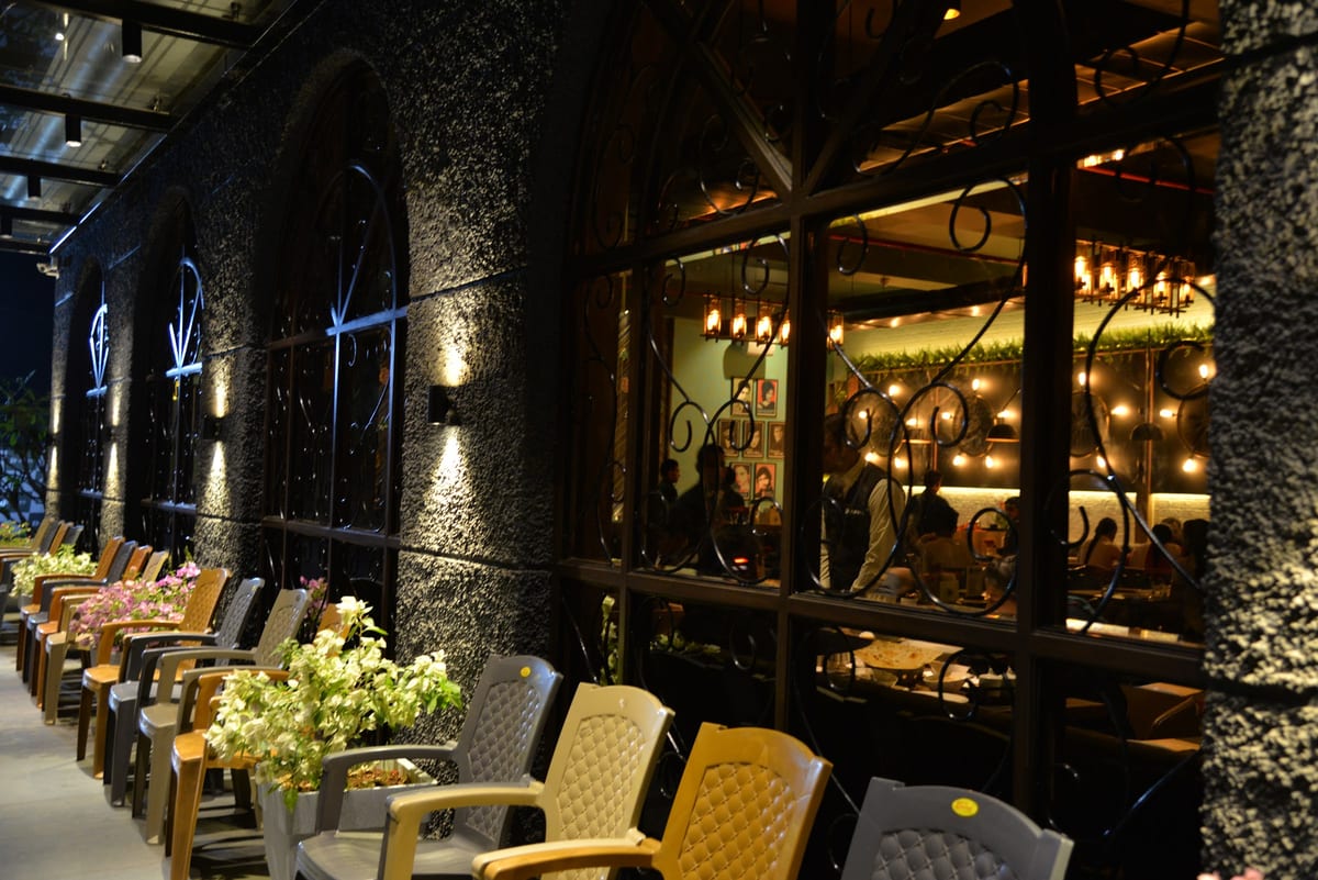 Outdoor tables beside a dark stone building with arched windows and warm interior lighting