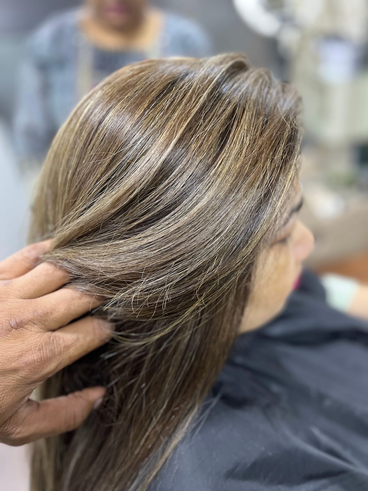 Stylist lifting a client's long highlighted hair in the salon