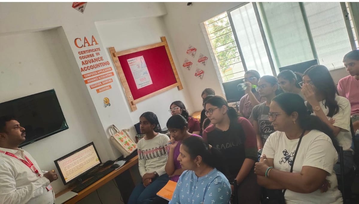 Instructor presenting to a seated group beside a computer display in a classroom
