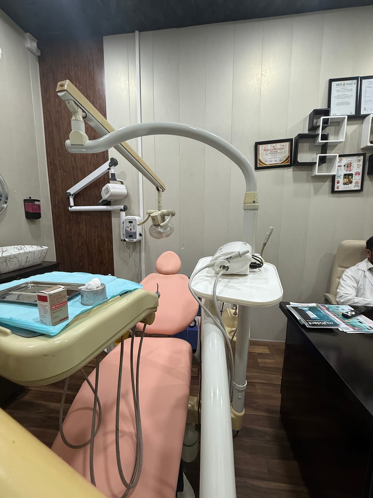 Treatment room with dental chair, overhead lamp, instruments and framed certificates on the wall