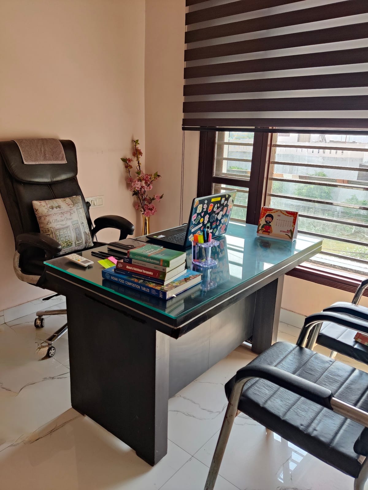 Office interior with a desk, chair, books and stationery beside a blinded window