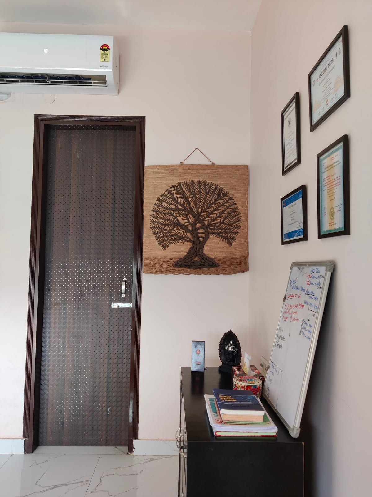 Interior corner with a screened door, tree wall hanging, framed certificates and a book shelf