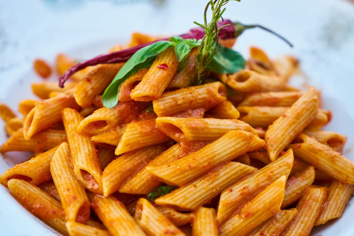 Plate of penne pasta in tomato sauce garnished with basil and herbs