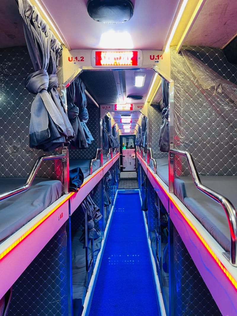 Sleeper bus corridor lined with curtained bunks, handrails and coloured lighting