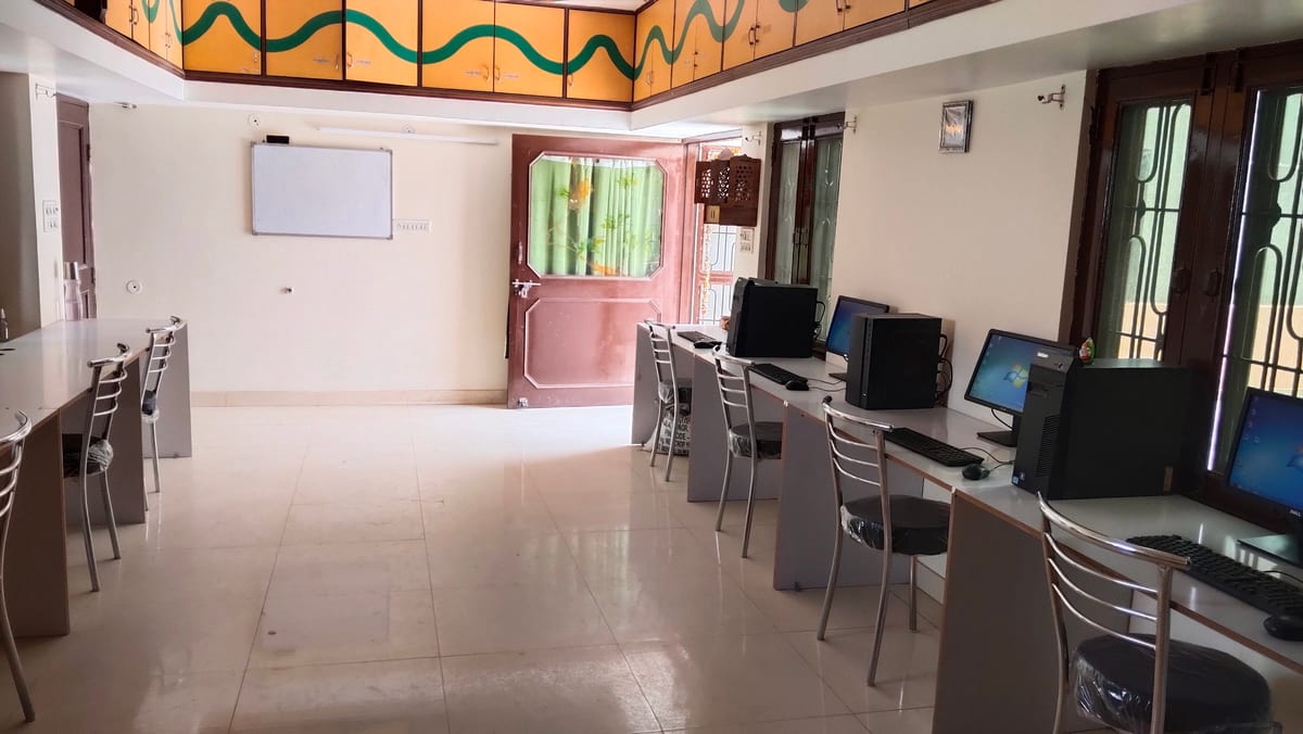 Computer lab with rows of monitors, desks, chairs and a curtained rear door