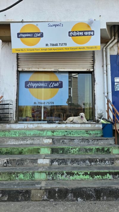 Yellow Happiness Club storefront sign above a glass entrance in Titwala East
