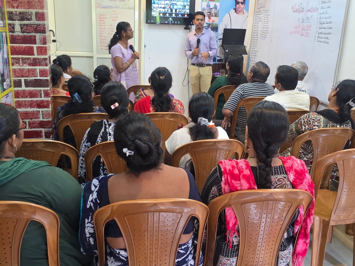 Two people presenting to a seated group in a small room with whiteboards