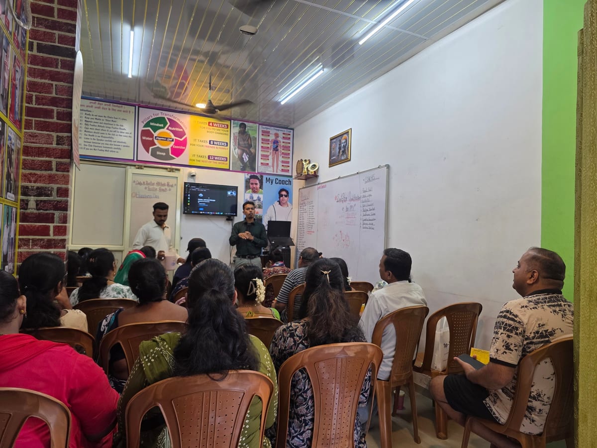Two coaches presenting to seated attendees in a classroom with posters and a whiteboard