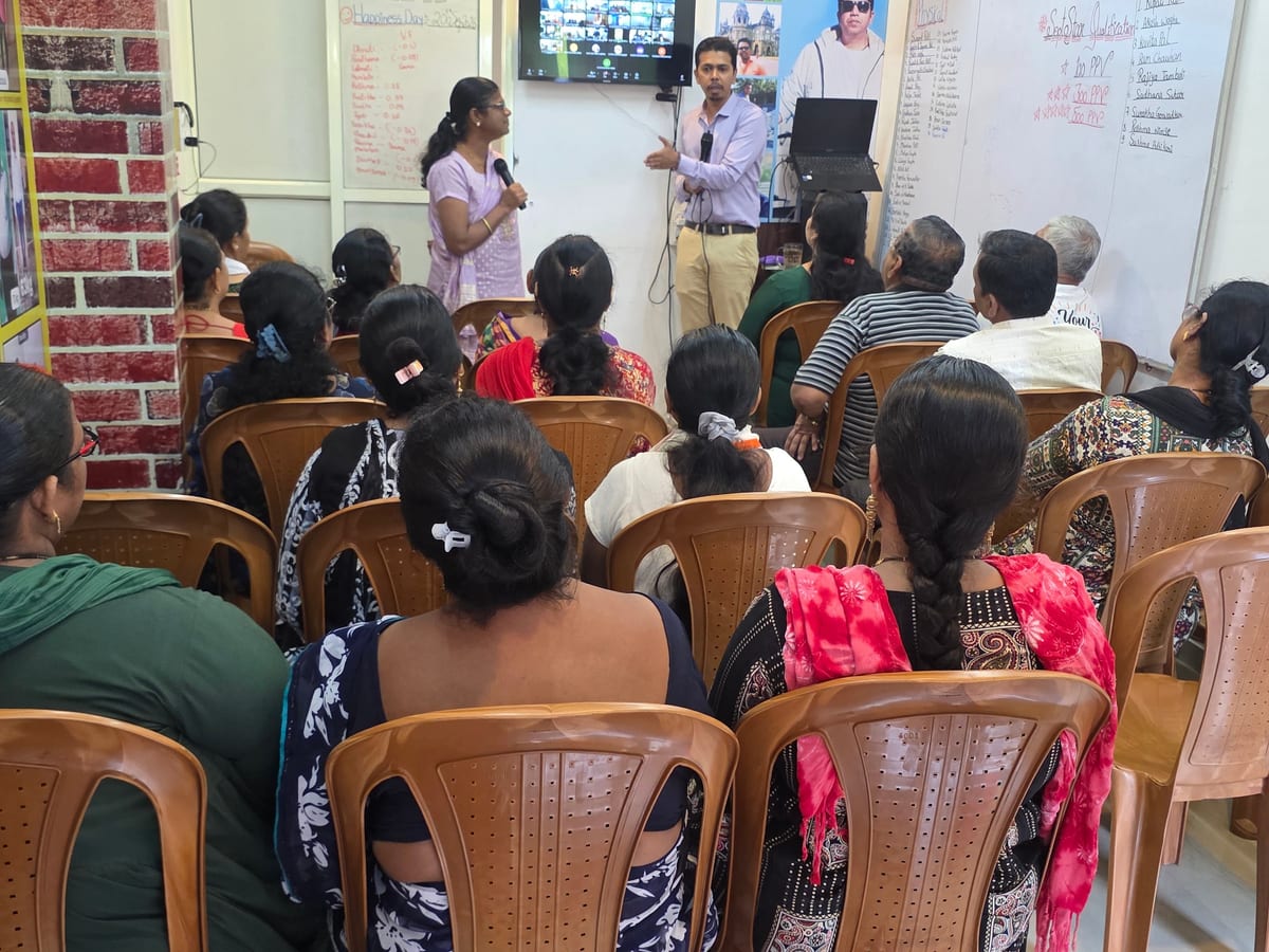 Two presenters addressing a seated audience in a classroom with a wall-mounted screen