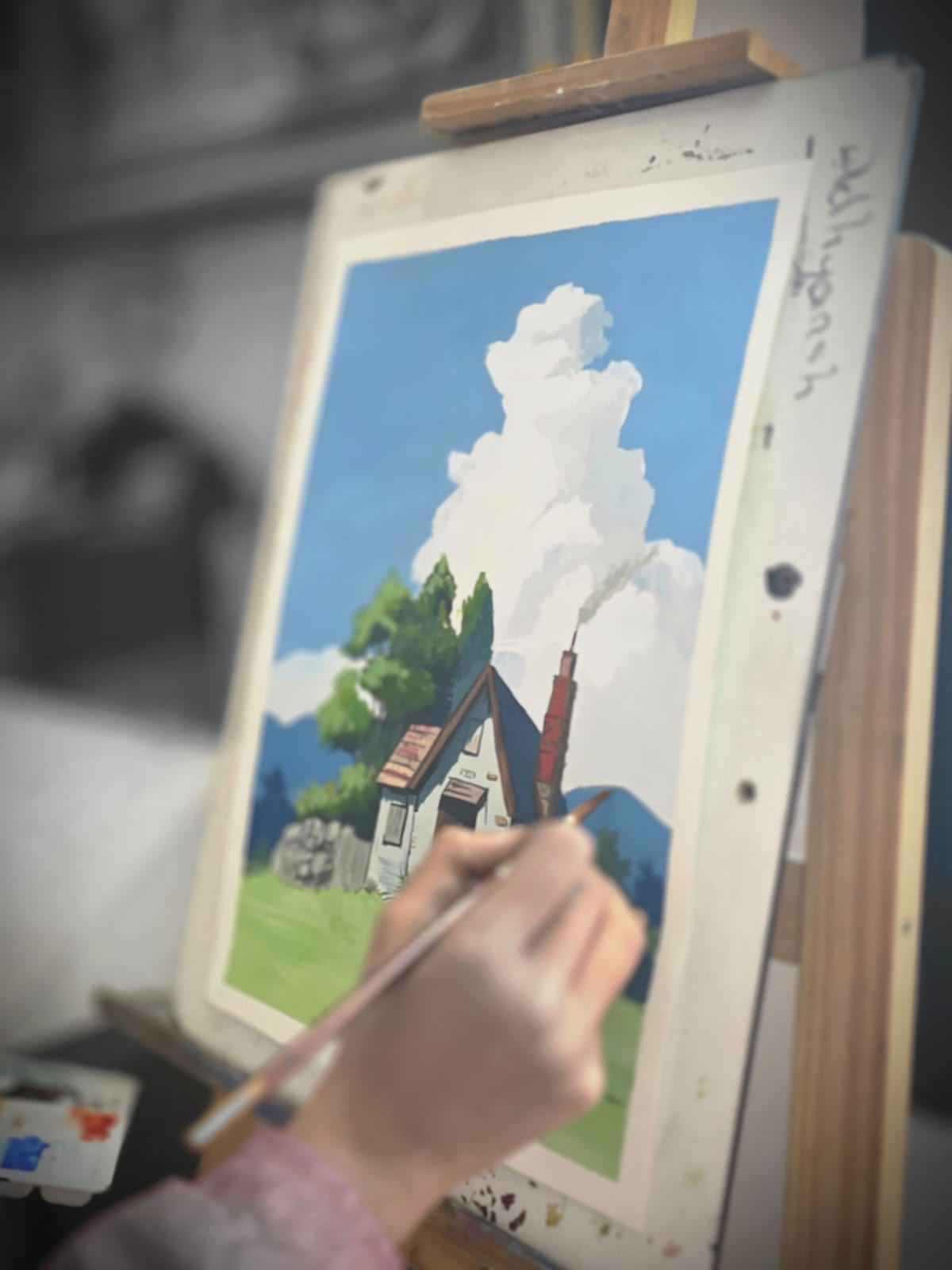 Hand applying paint to a landscape painting on a canvas easel