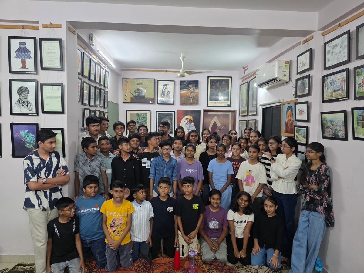 Group of children and adults posing in a gallery room surrounded by framed artwork at KD Art Academy Nagpur