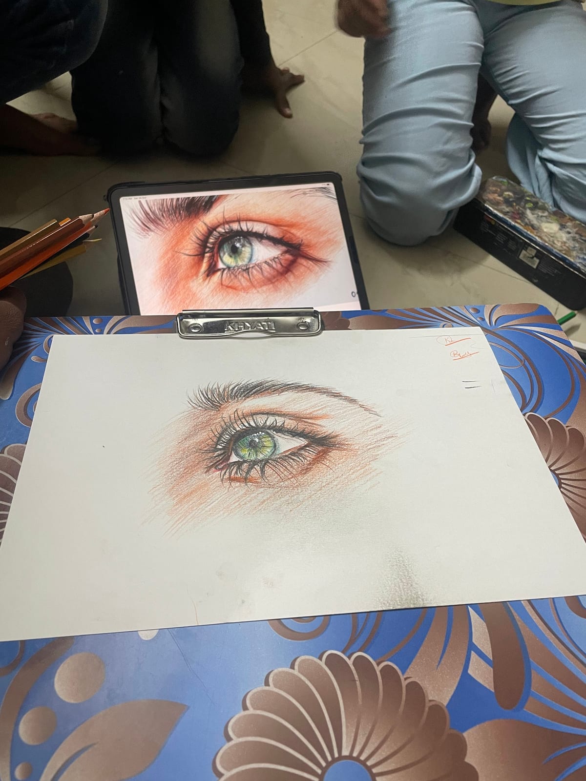 Hand-drawn eye on a clipboard beside a tablet showing an eye reference image