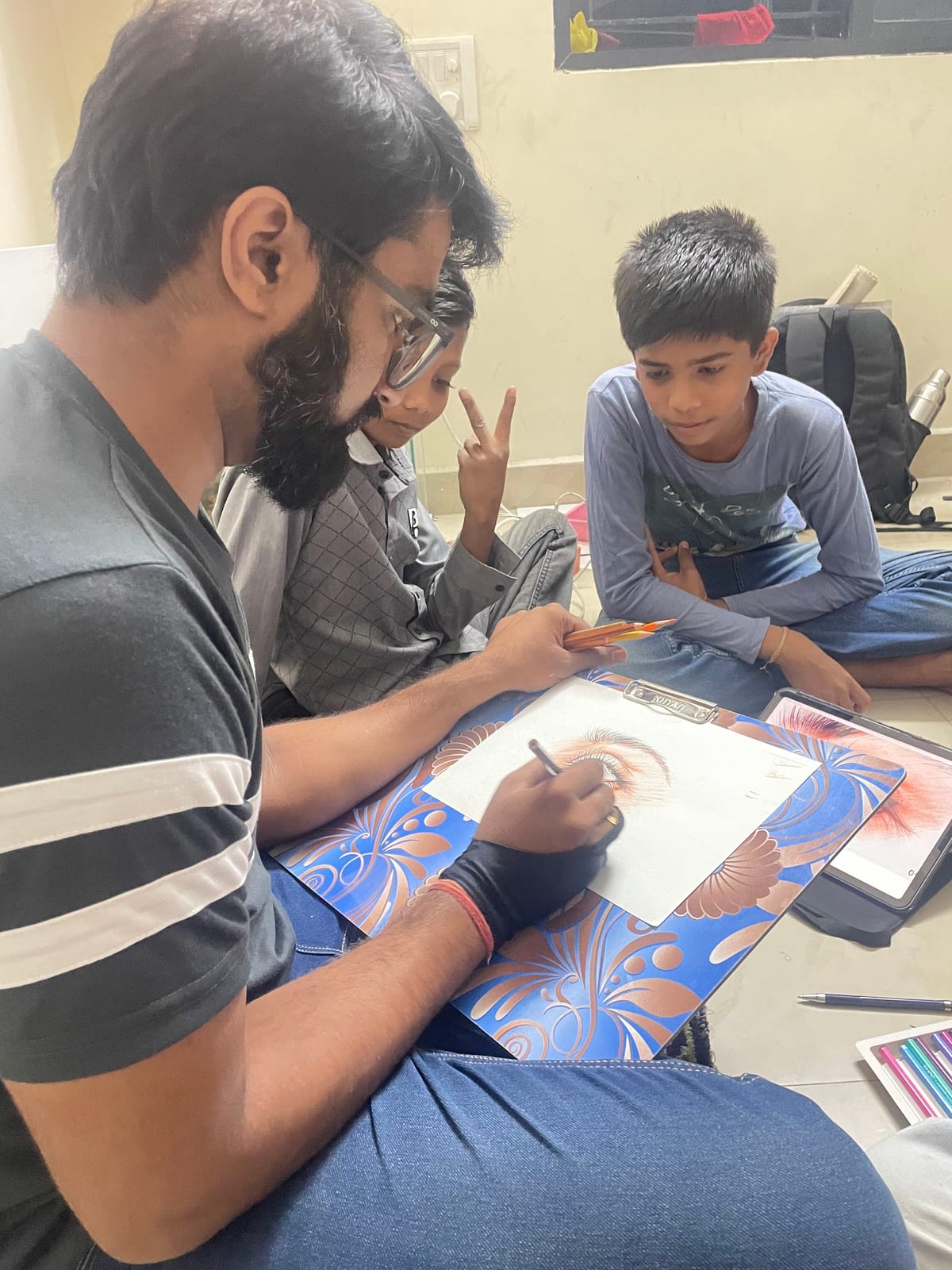 Man drawing on paper at a table while two children watch